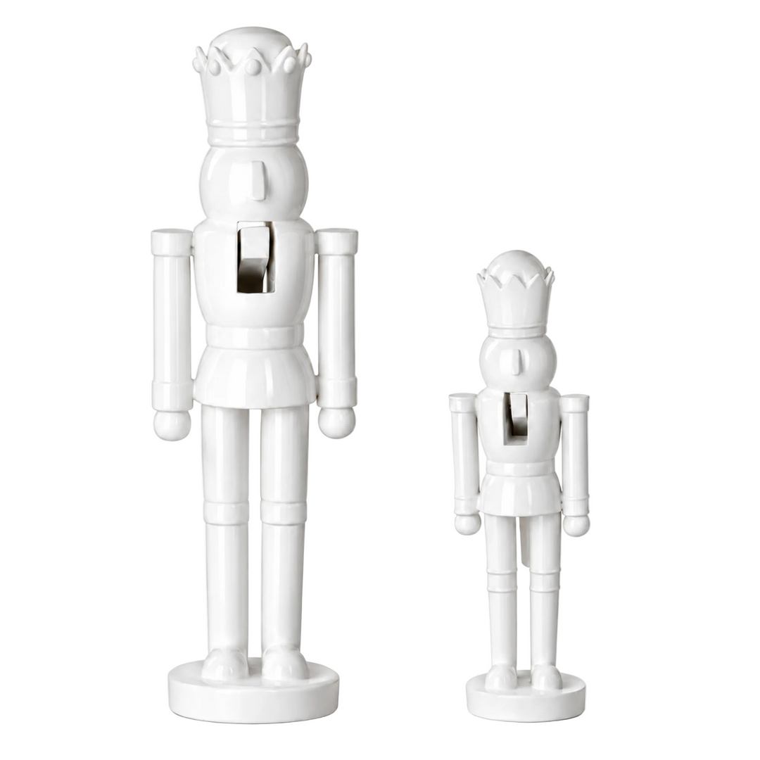 Two white ceramic nutcracker figurines, one large and one small, standing on round bases against a plain white background.