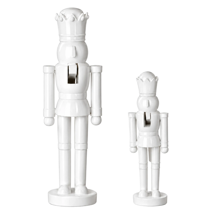 Two white ceramic nutcracker figurines, one large and one small, standing on round bases against a plain white background.