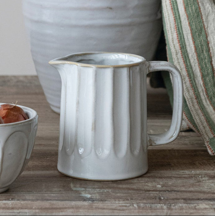 Set of ceramic items including a pitcher, bowl, and cup on a wooden surface with a striped towel.