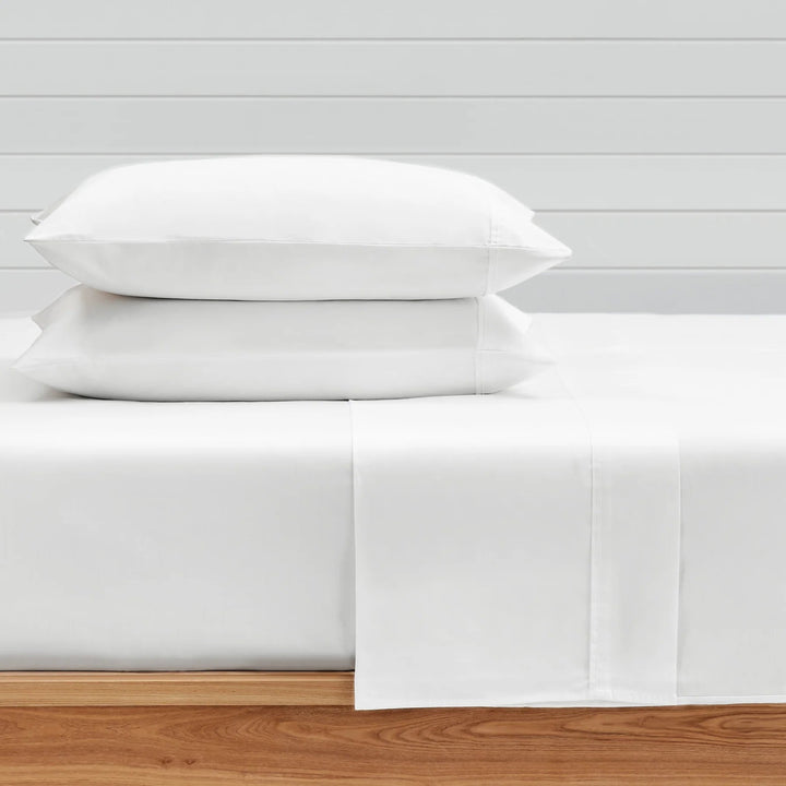 White bed sheets and pillows on a wooden bed frame with a light gray wall background