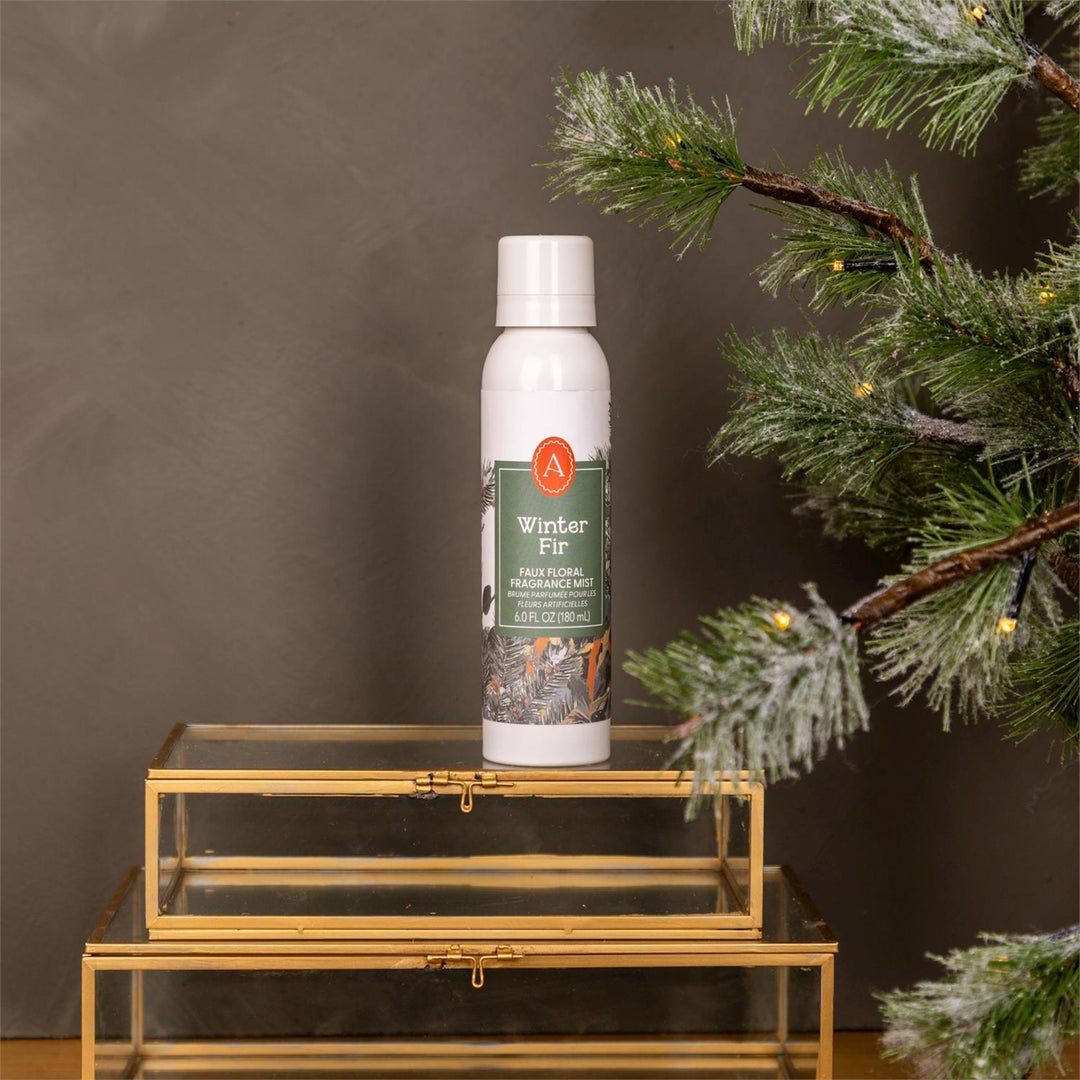 White spray bottle labeled 'Winter Fit' on a gold stand with a Christmas tree in the background