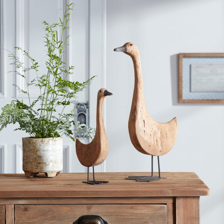 Two wooden goose sculptures on a wooden surface with a plant in the background.