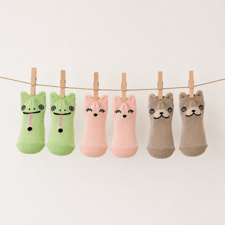 Five pairs of novelty baby socks with animal faces are hanging from a string with wooden clothespins against a plain white background.