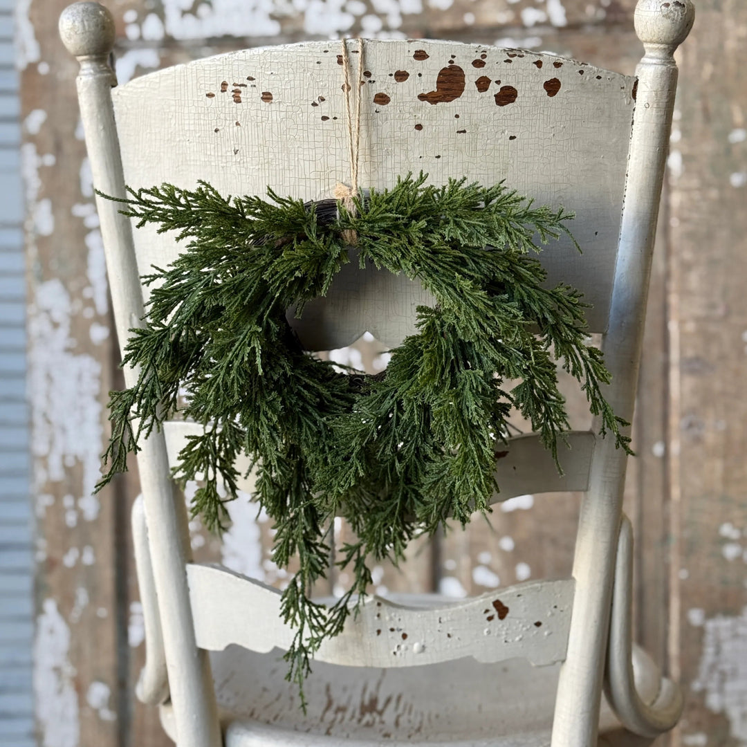 Green wreath hanging on a white wooden chair against a rustic wooden wall.