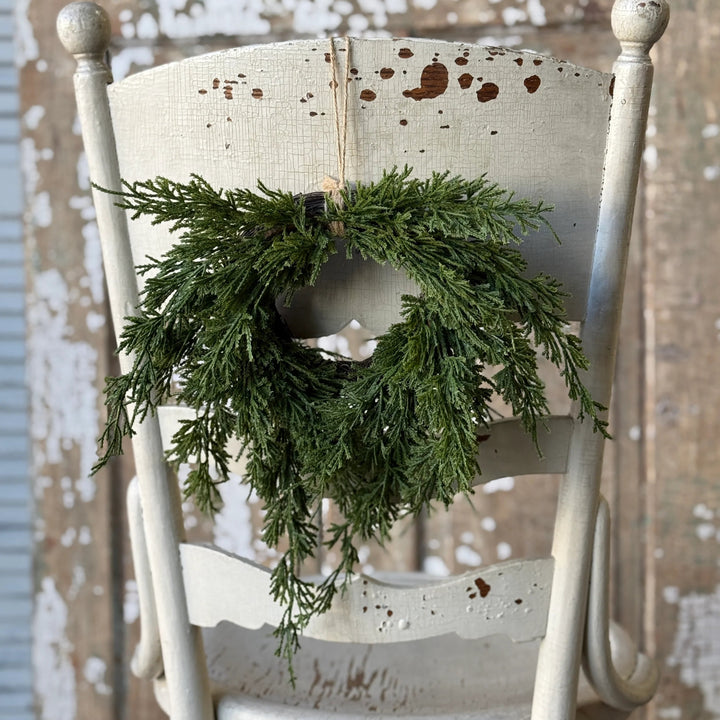 Green wreath hanging on a white wooden chair against a rustic wooden wall.