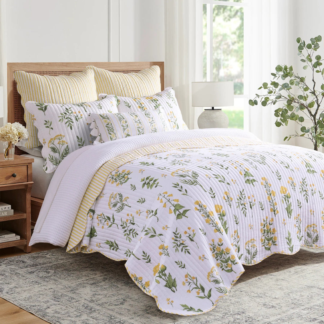 Floral bedding set on a bed in a bright bedroom with a lamp and plant.