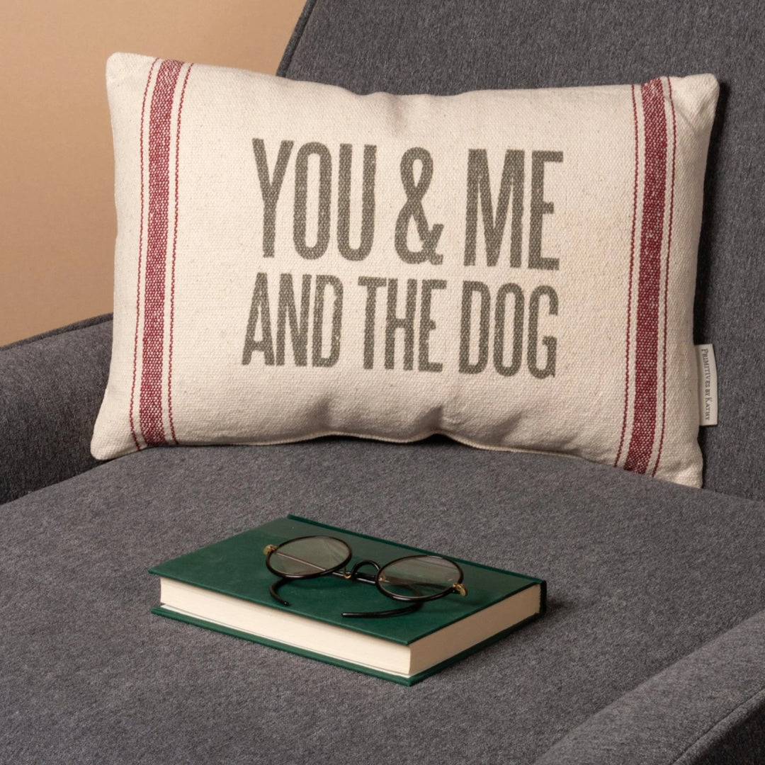 Decorative pillow with 'You & Me And The Dog' text on a gray couch with a book and glasses.