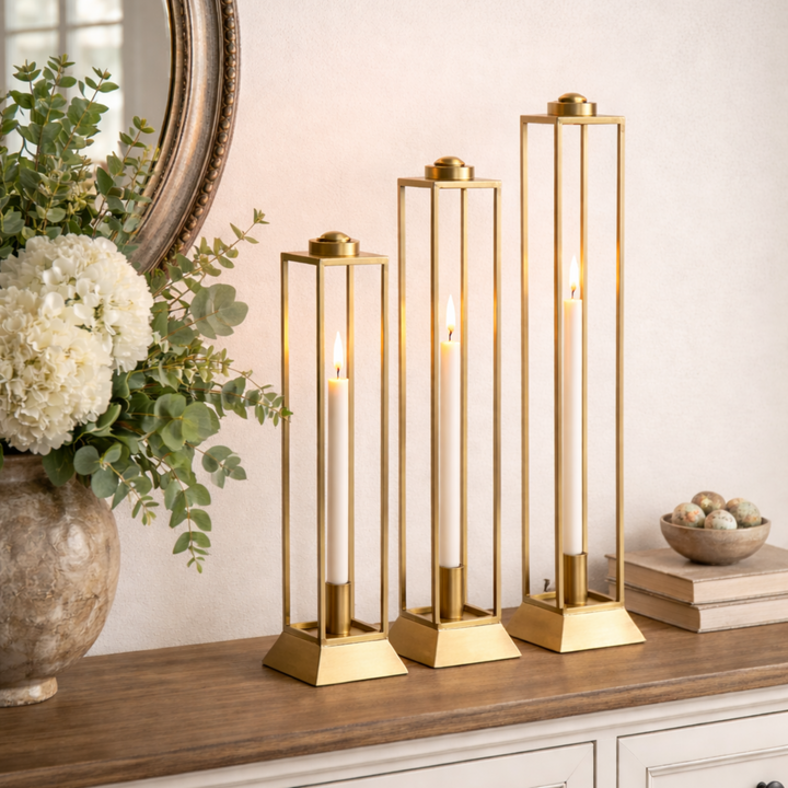 Decorative gold candle holders on a wooden surface with a mirror and flowers in the background.