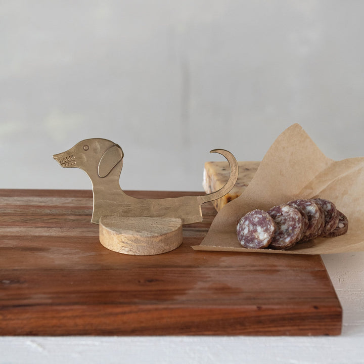 Wooden dachshund-shaped cutting board with sliced salami on a wooden surface.