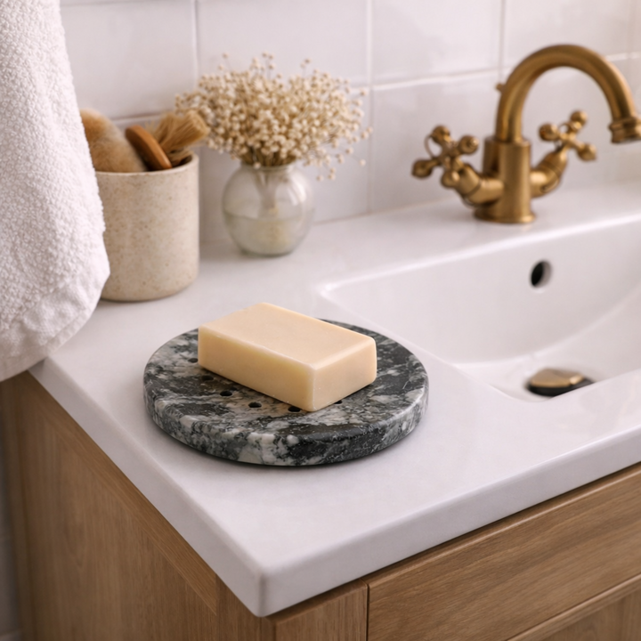 Bar of soap on a marble soap dish on a bathroom counter with a sink and faucet in the background.