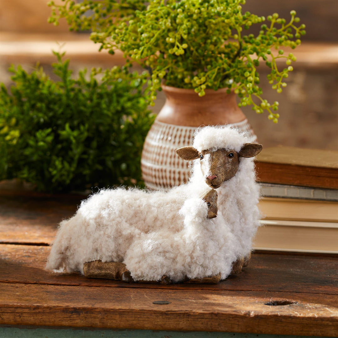 mother sheep and lamb plush figurine on a wooden table with faux plants in the background