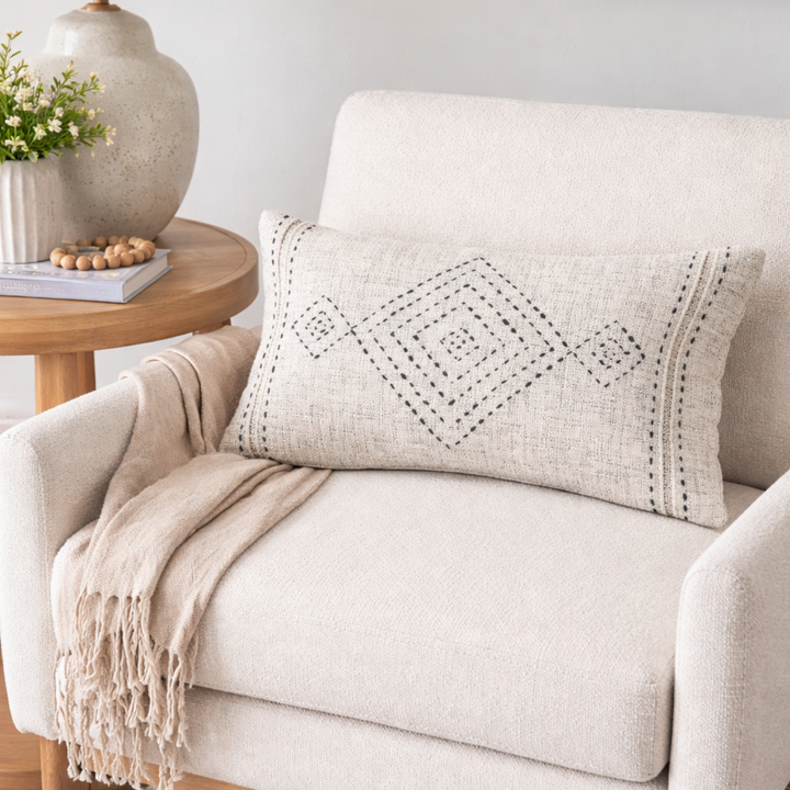 Beige armchair with a decorative pillow and lamp in a cozy living room setting