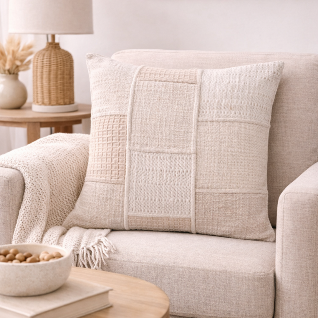 Beige textured pillow on a beige sofa with a lamp and decor items in the background.