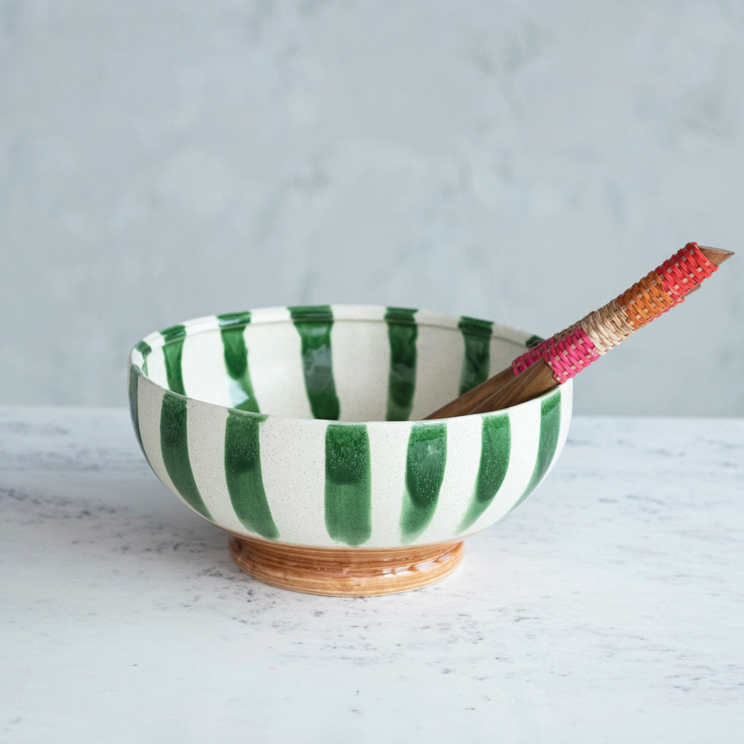 Green and white striped ceramic bowl with a wooden spoon on a light gray background