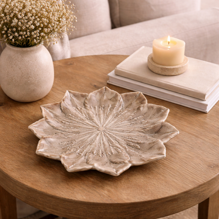 Decorative stoneware plate on a wooden table with a candle and vase in the background.