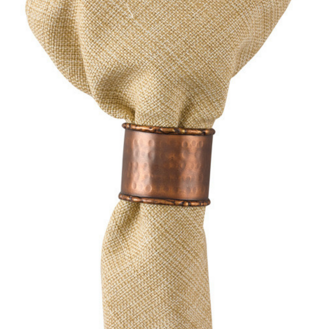 A beige cotton napkin with a hammered copper napkin ring attached.